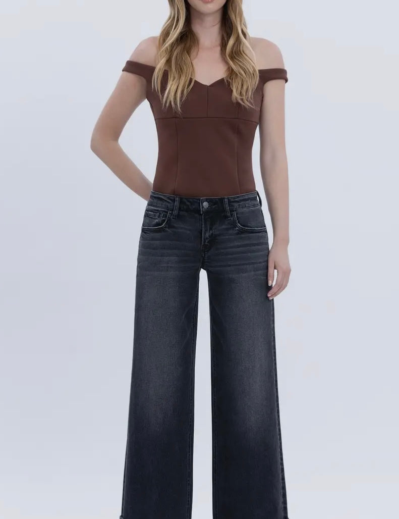 Woman wearing a brown off-shoulder top and black wide-leg jeans on a white background