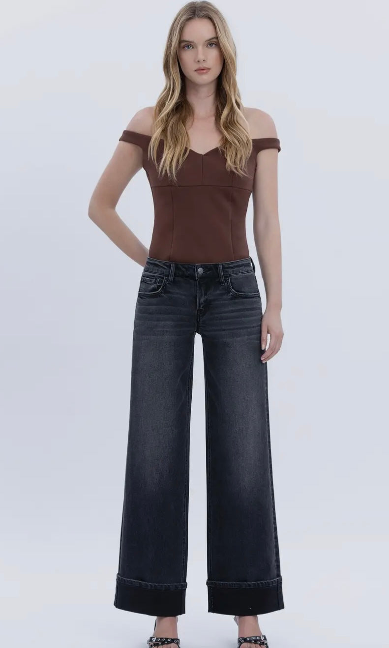 Woman wearing a brown off-shoulder top and black wide-leg jeans on a white background