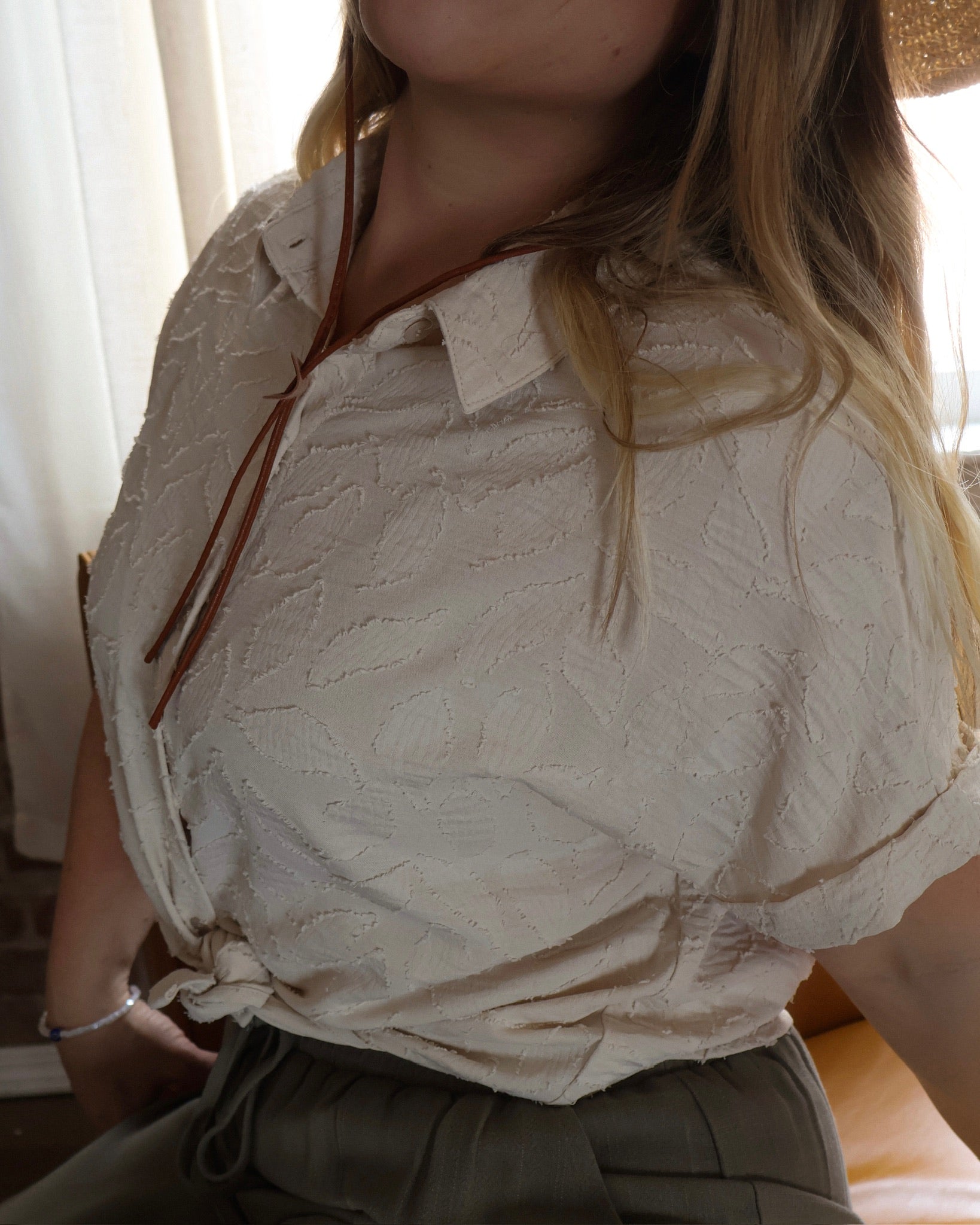 Person wearing a textured beige blouse with a blurred background