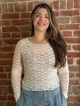 Woman wearing a sheer lace top and blue jeans against a brick wall.