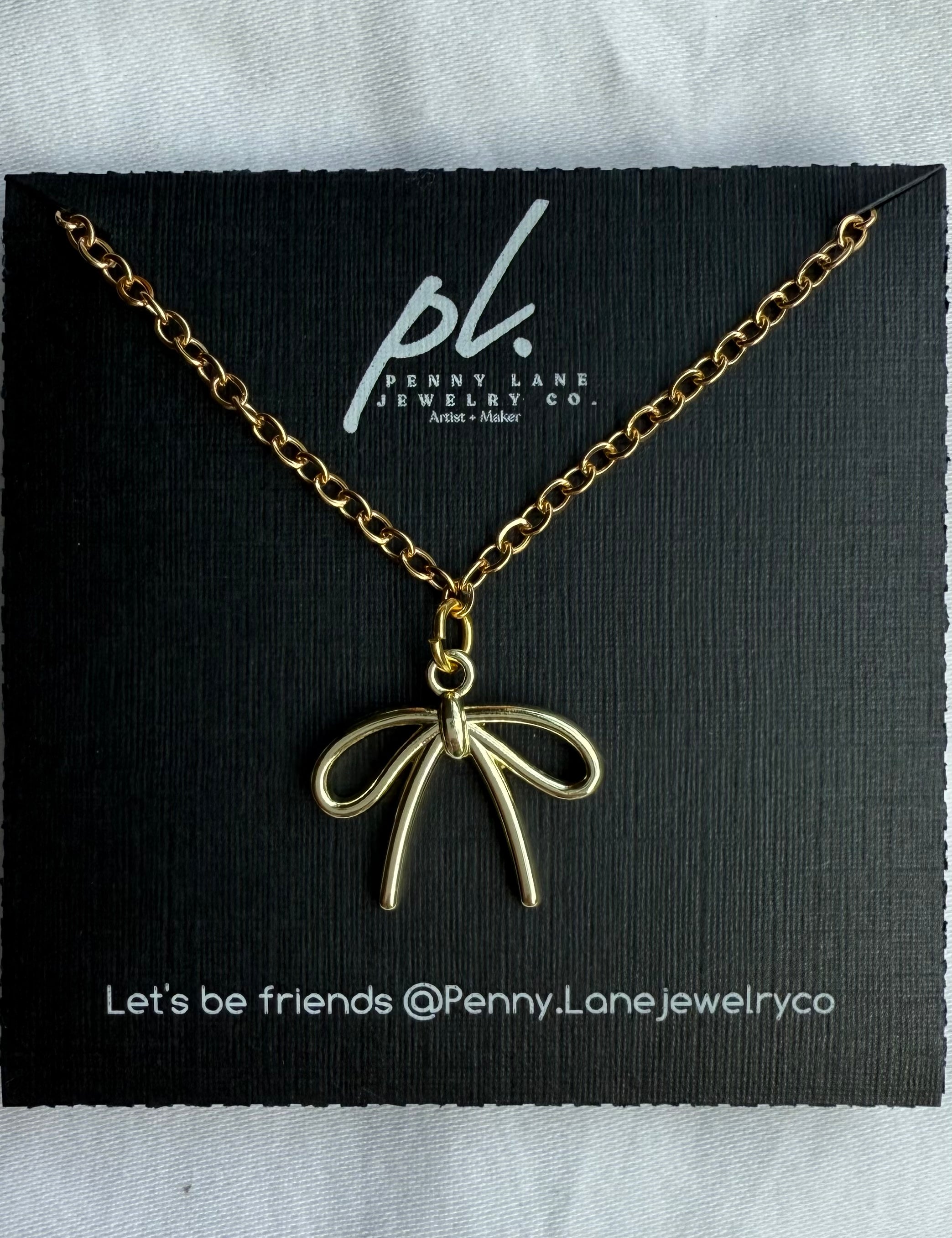 Gold necklace with Bow pendant on a Penny Lane Jewelry Co. card.