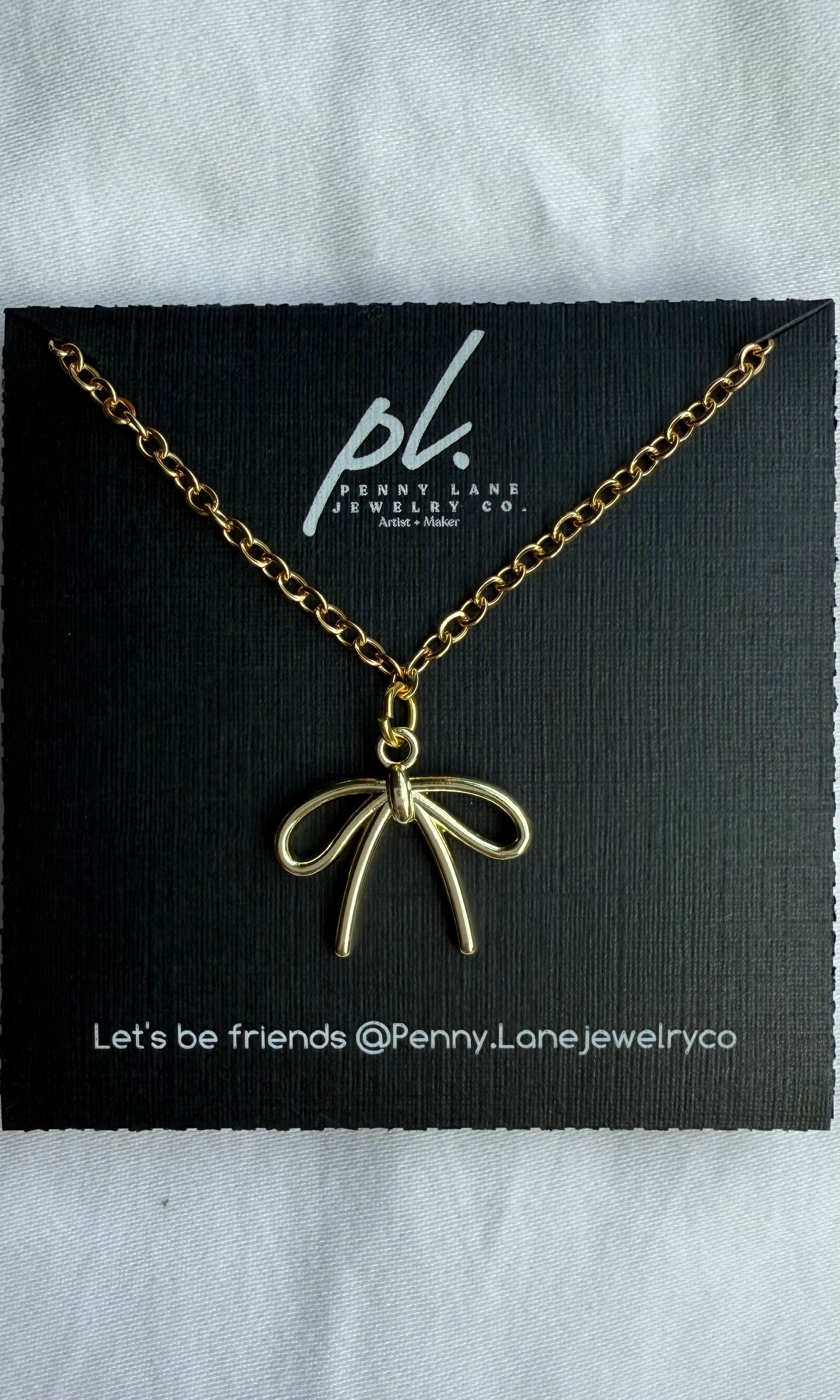 Gold necklace with Bow pendant on a Penny Lane Jewelry Co. card.