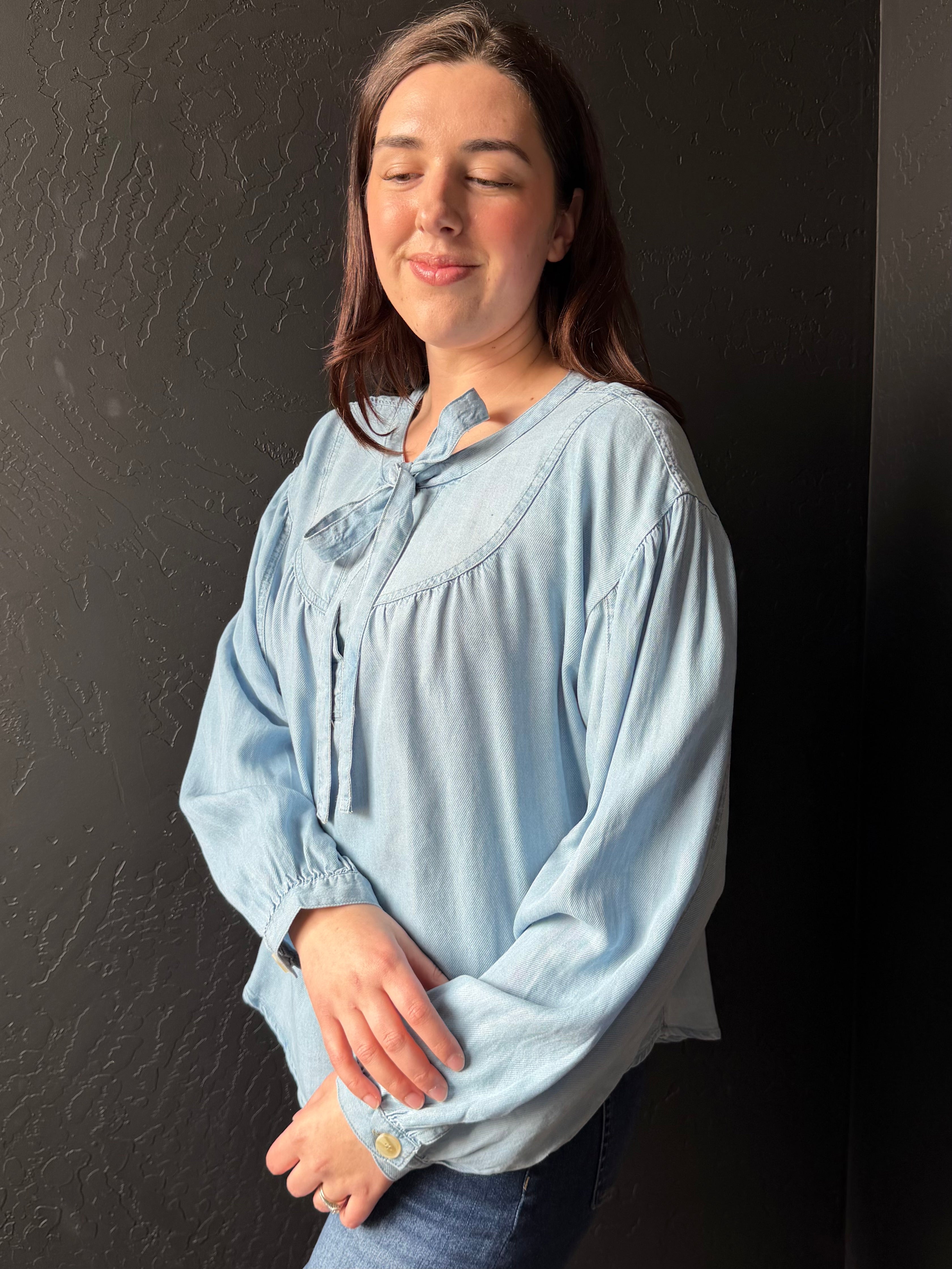 Woman wearing a light blue blouse against a dark background